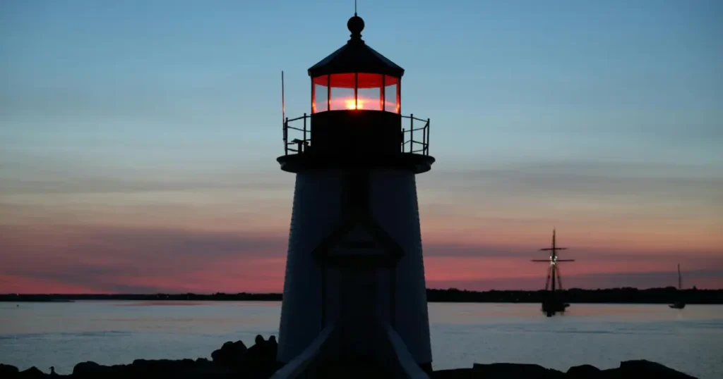 Brant Point Lighthouse in Nantucket during a picturesque sunset with a ship in the background.