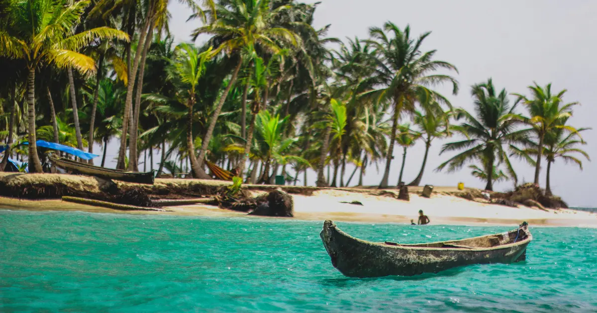 A traditional wooden canoe floating in turquoise waters with palm trees in the background at the San Blas Islands, Panama.