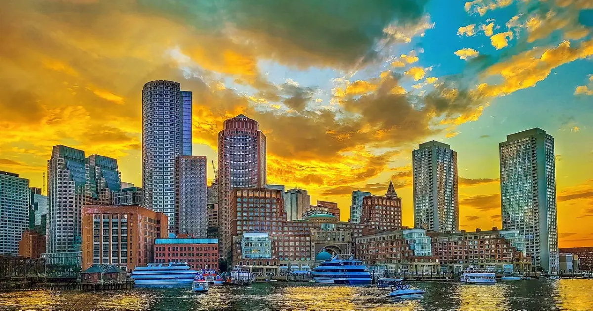 Stunning view of the Boston skyline during sunset with vibrant orange and yellow hues reflecting on the buildings and water.