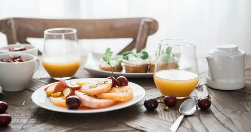 A rustic breakfast table with fresh fruits, cherries, orange juice, and pastries, representing Costa Rican cuisine.