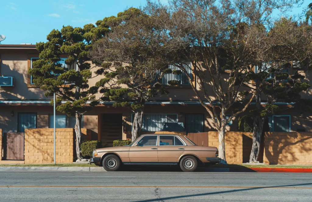 A vintage brown car parked in front of a classic Beverly Hills home.