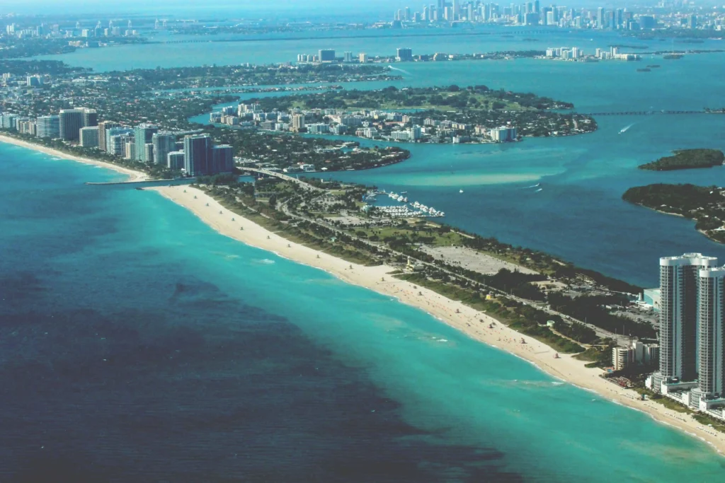 A panoramic aerial view of Miami's coastline, featuring turquoise waters, sandy beaches, and urban skylines