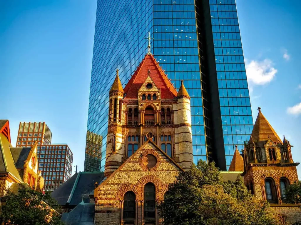 Boston's historic Trinity Church juxtaposed against a modern glass skyscraper under a clear blue sky.