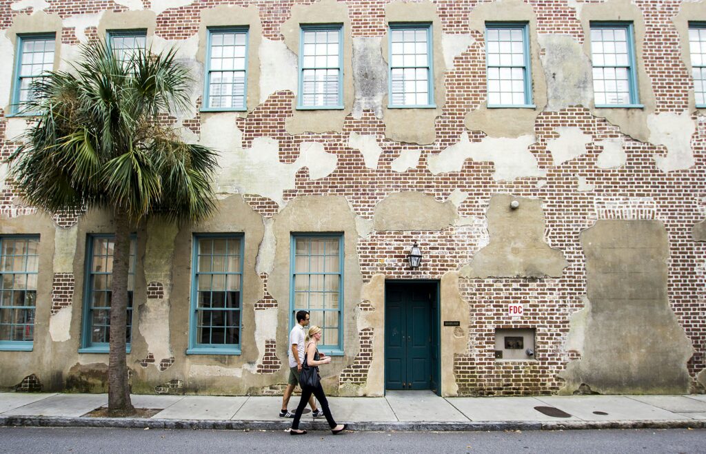 A historic brick building with blue window frames and a palm tree on a street in Charleston, SC. showcasing Best Pet-Friendly Hotels