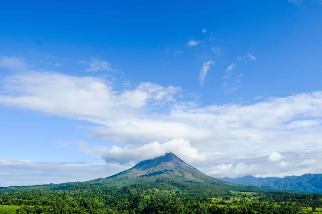 The majestic Arenal Volcano rising above lush green forests under a bright blue sky in Costa Rica.