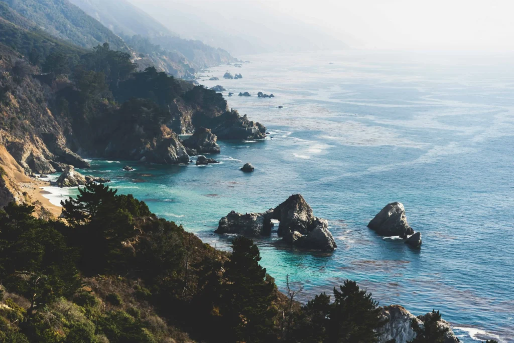 Rocky shoreline and turquoise waters of Big Sur with lush greenery.