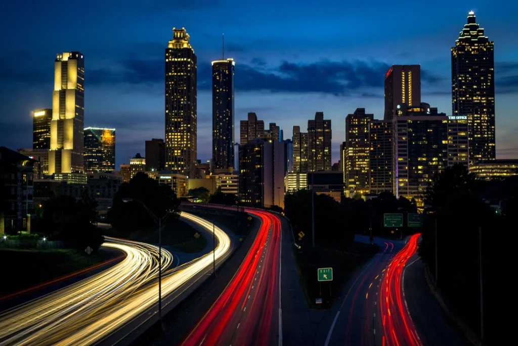 The Atlanta skyline lit up at night, viewed from Jackson Street Bridge with light trails.