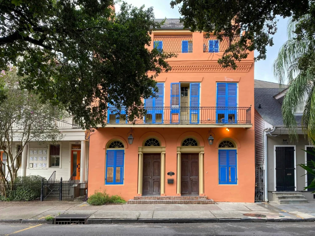 A bright orange Creole-style home in New Orleans with blue shutters and arched windows with boutique hotels new orleans nearby