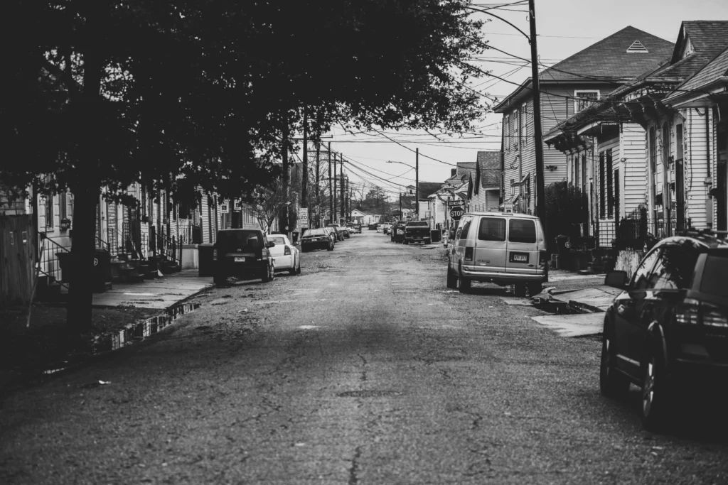 A black-and-white photo of a quiet residential street in New Orleans, lined with cars and houses.