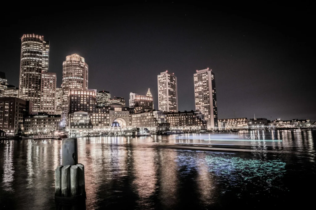 Illuminated Boston skyline reflecting on the water at night with city lights creating a serene ambiance.