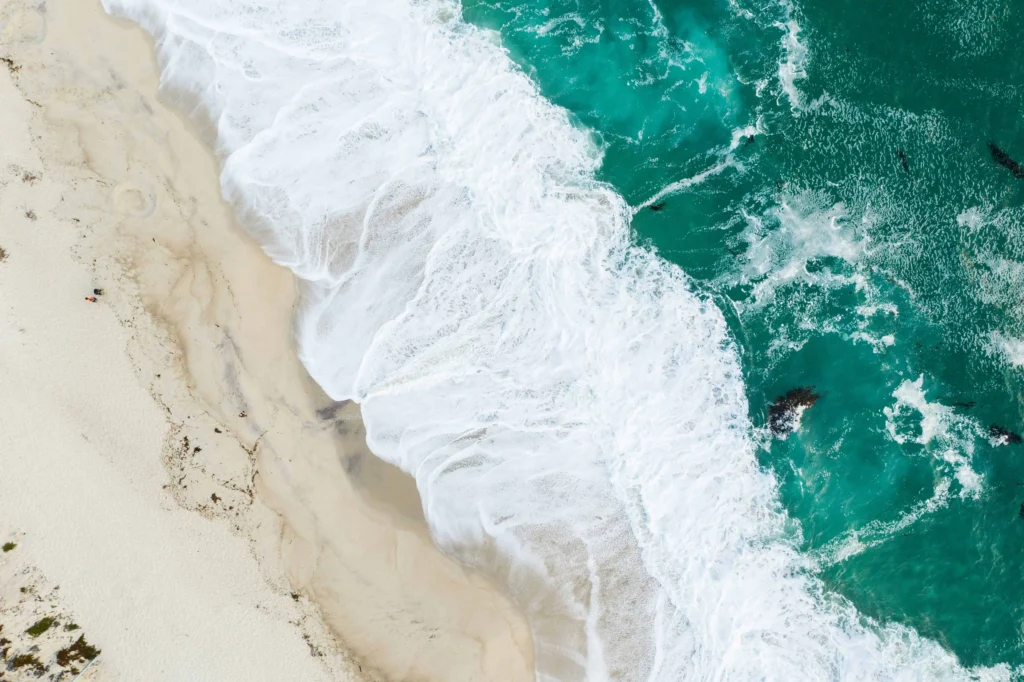 Aerial view of turquoise waves meeting the sandy shores at Carmel Beach.