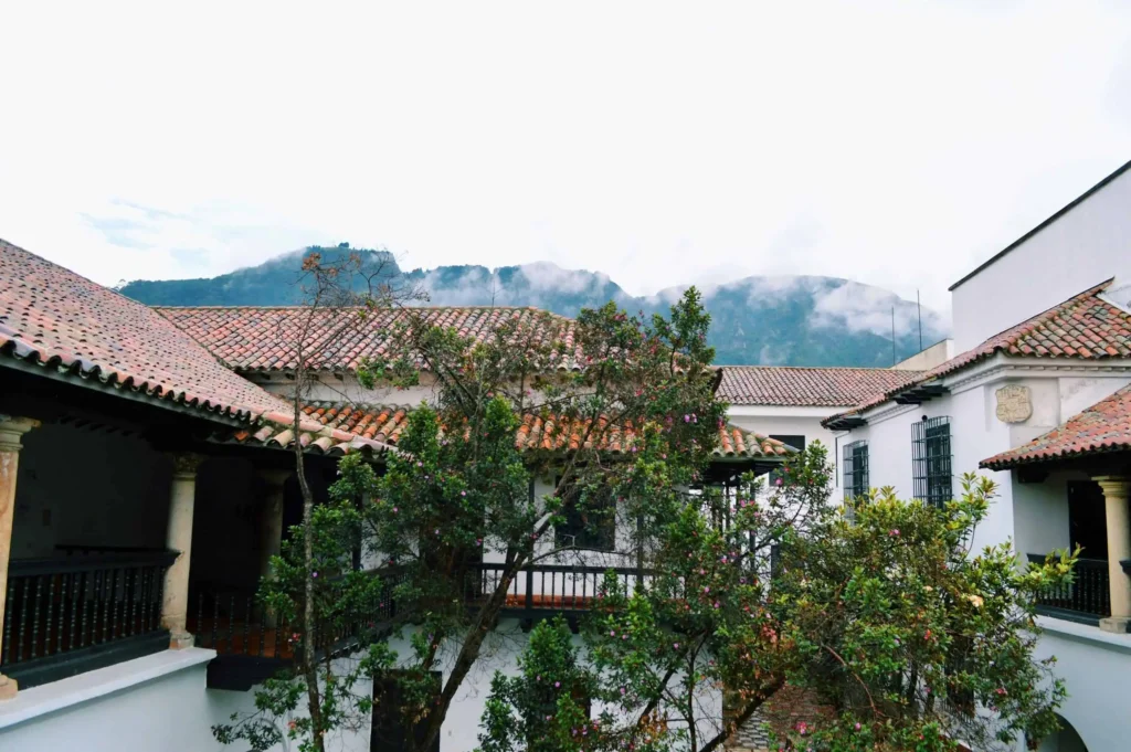 Traditional colonial-style courtyard in Bogota, with red-tiled roofs and lush greenery against a mountain backdrop