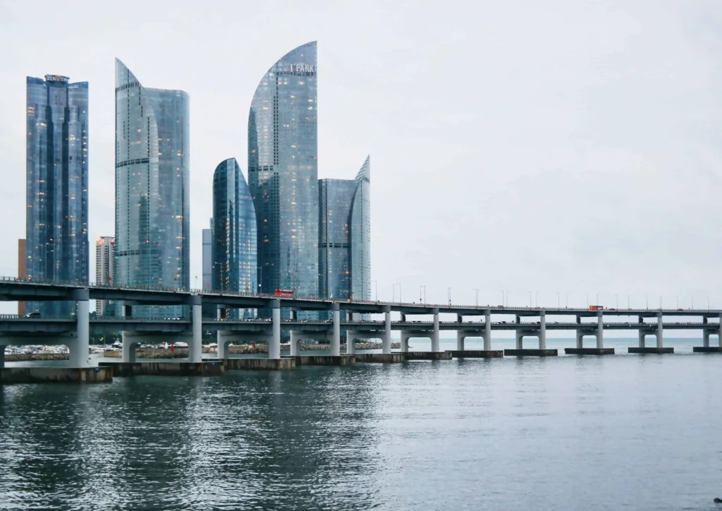 Iconic skyscrapers and bridges of Busan reflecting on the water at dusk.
