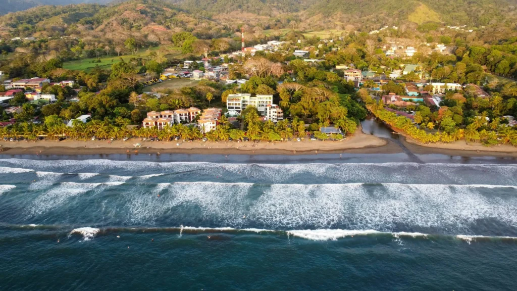 A vibrant aerial view of Jaco Beach, showcasing the shoreline, waves, and nearby greenery.