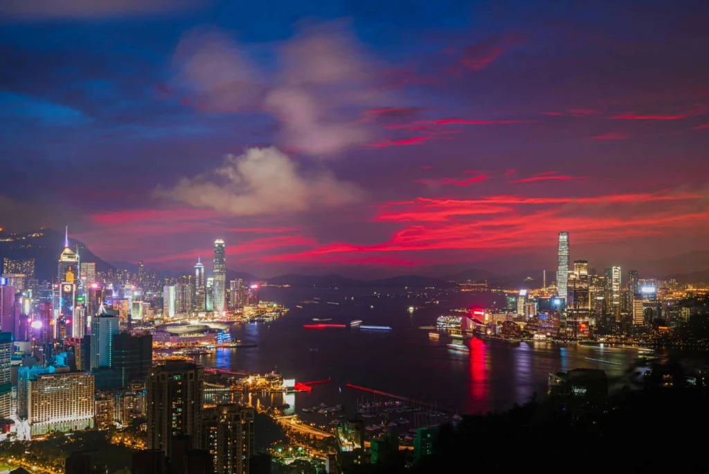 Nighttime view of the Hong Kong skyline with vibrant lights reflecting over Victoria Harbour.