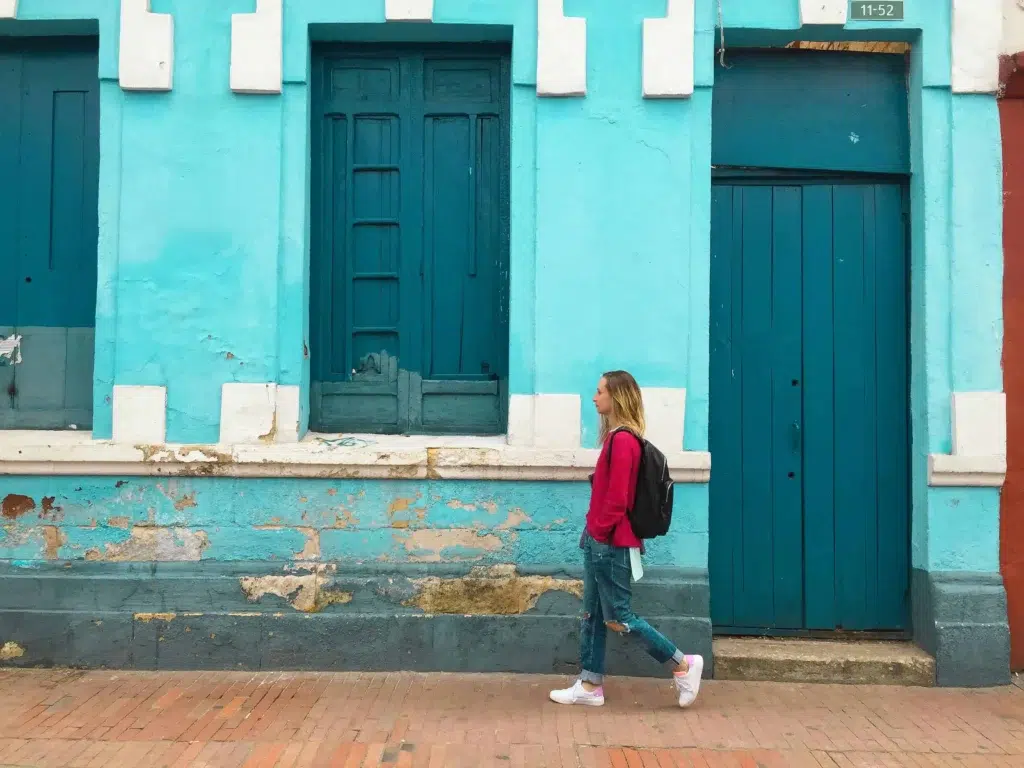 A tourist walking past a bright turquoise building in La Candelaria, Bogota.