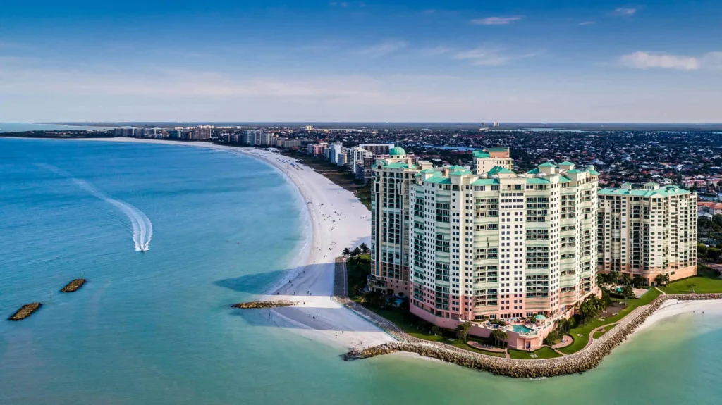 An aerial view of Marco Island’s coastline with beachfront buildings and turquoise waters.