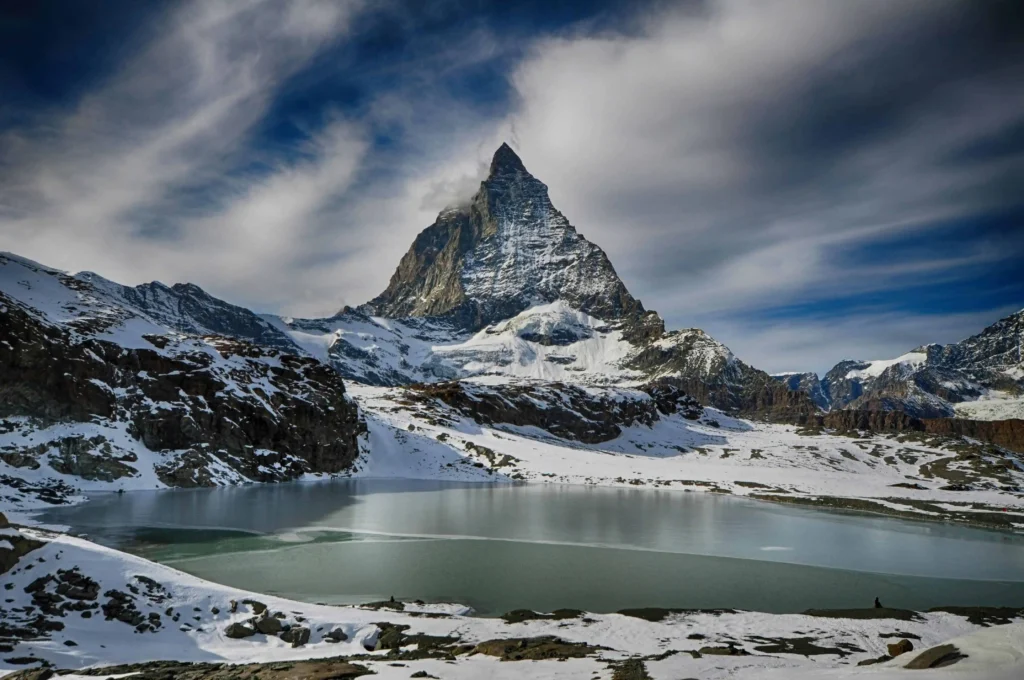 The Matterhorn mountain reflected in a partially frozen lake during winter.