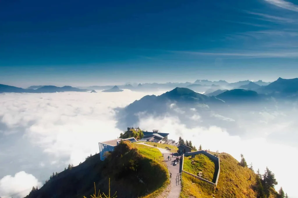 A panoramic view from a mountaintop in Switzerland, overlooking a sea of clouds with distant peaks in the horizon.