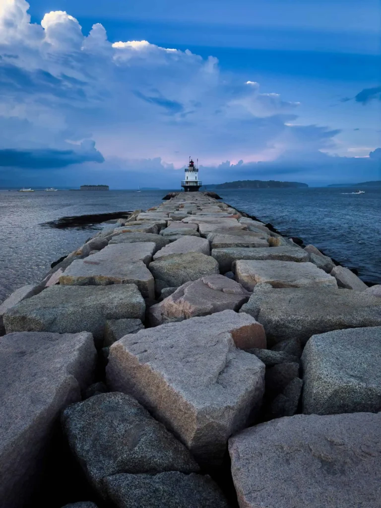 A stone pathway leading to a lighthouse under a vivid blue sky.