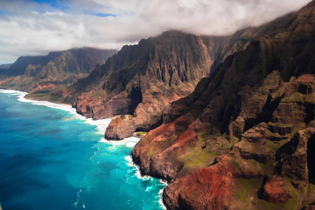 Aerial view of the Na Pali Coast’s rugged cliffs and blue waters in Kauai.