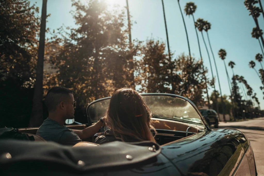 A couple driving a vintage convertible through Beverly Hills under the golden sunlight.