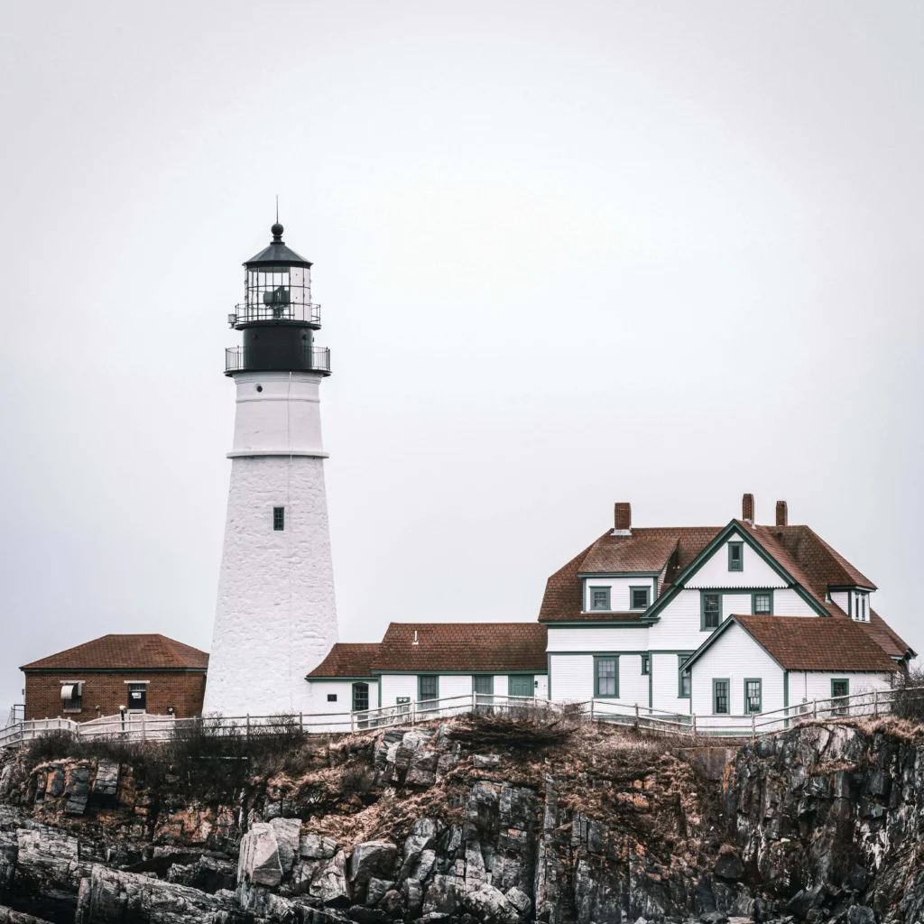 Portland Head Light lighthouse with an adjacent historic building on a rocky coastline.