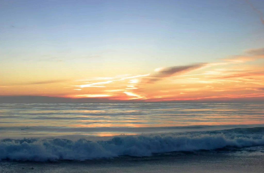 A serene sunset with waves and golden skies over the Pacific Ocean.