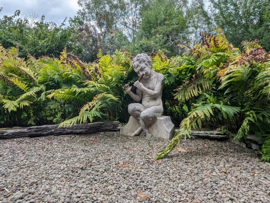 A stone statue of a musician surrounded by lush ferns in a secret garden in Cooperstown, NY.