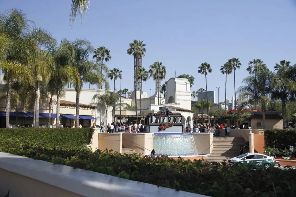 A view of Universal Studios Hollywood entrance with its iconic sign, fountain, and palm trees under a clear blue sky.