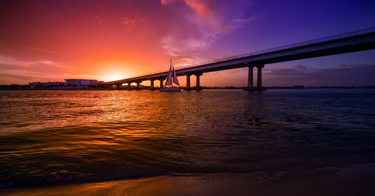 A stunning sunset over Perdido Pass bridge in Orange Beach, Alabama, with a sailboat in the water.