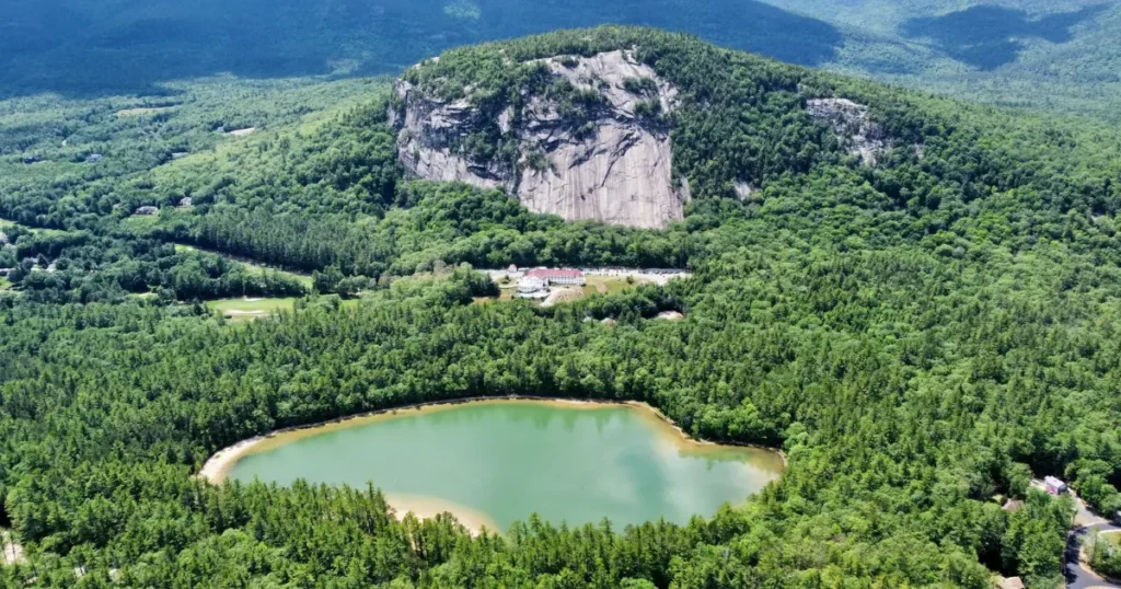 A scenic aerial view of Echo Lake and Cathedral Ledge in North Conway, NH, surrounded by lush green forests.