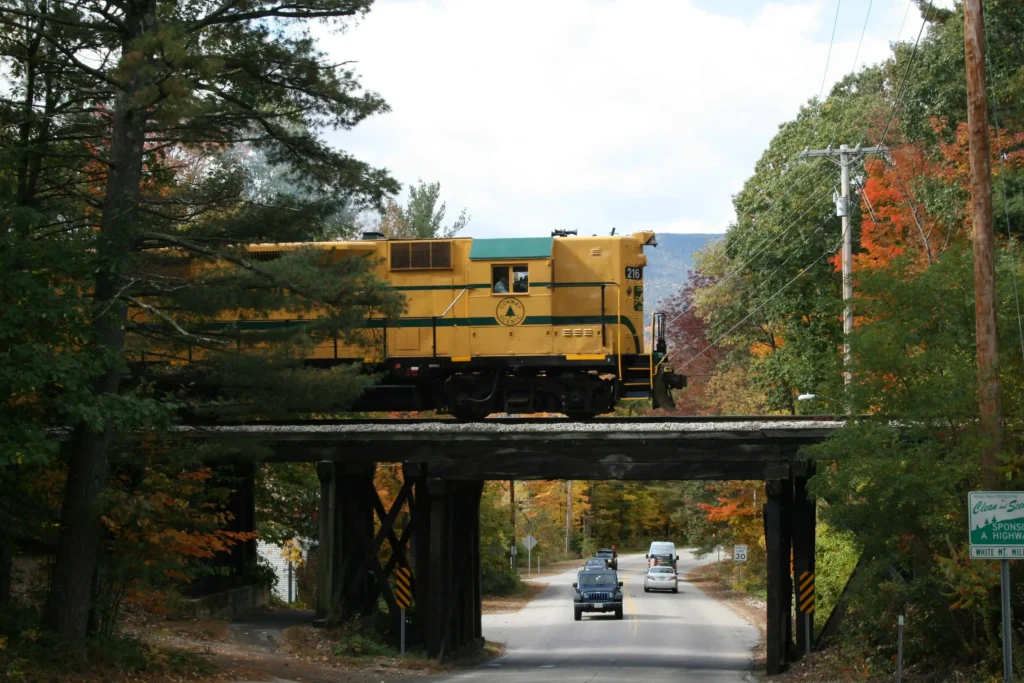 A vintage yellow locomotive of the Conway Scenic Railroad crossing a wooden bridge in North Conway, NH.