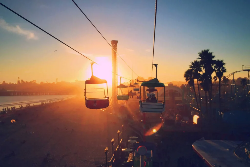 A sunset view of the Santa Cruz Beach Boardwalk with sky gliders and amusement rides.